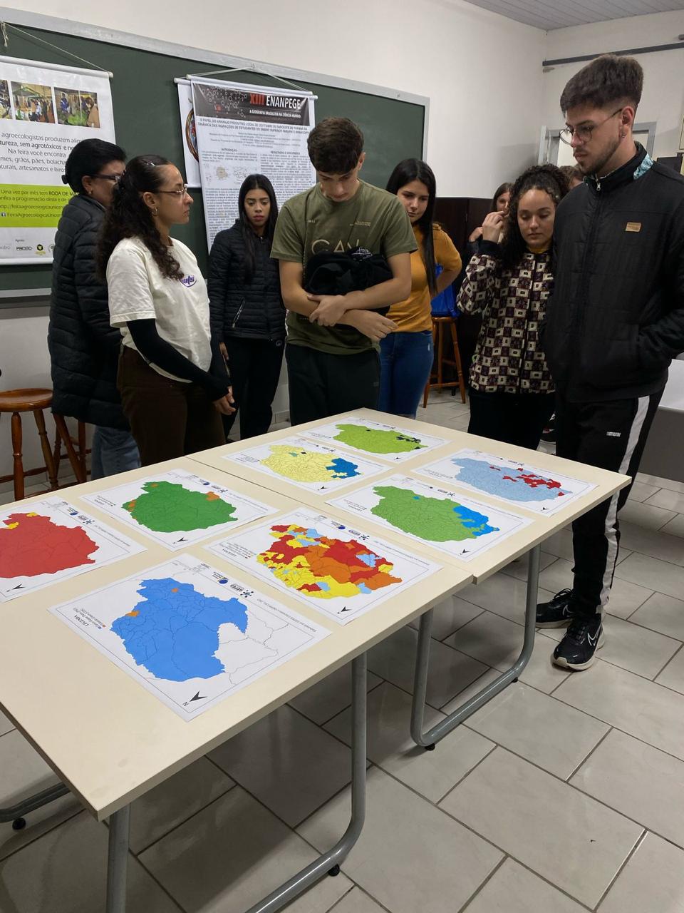 Estudantes observam mapas eleitorais dispostos sobre uma mesa